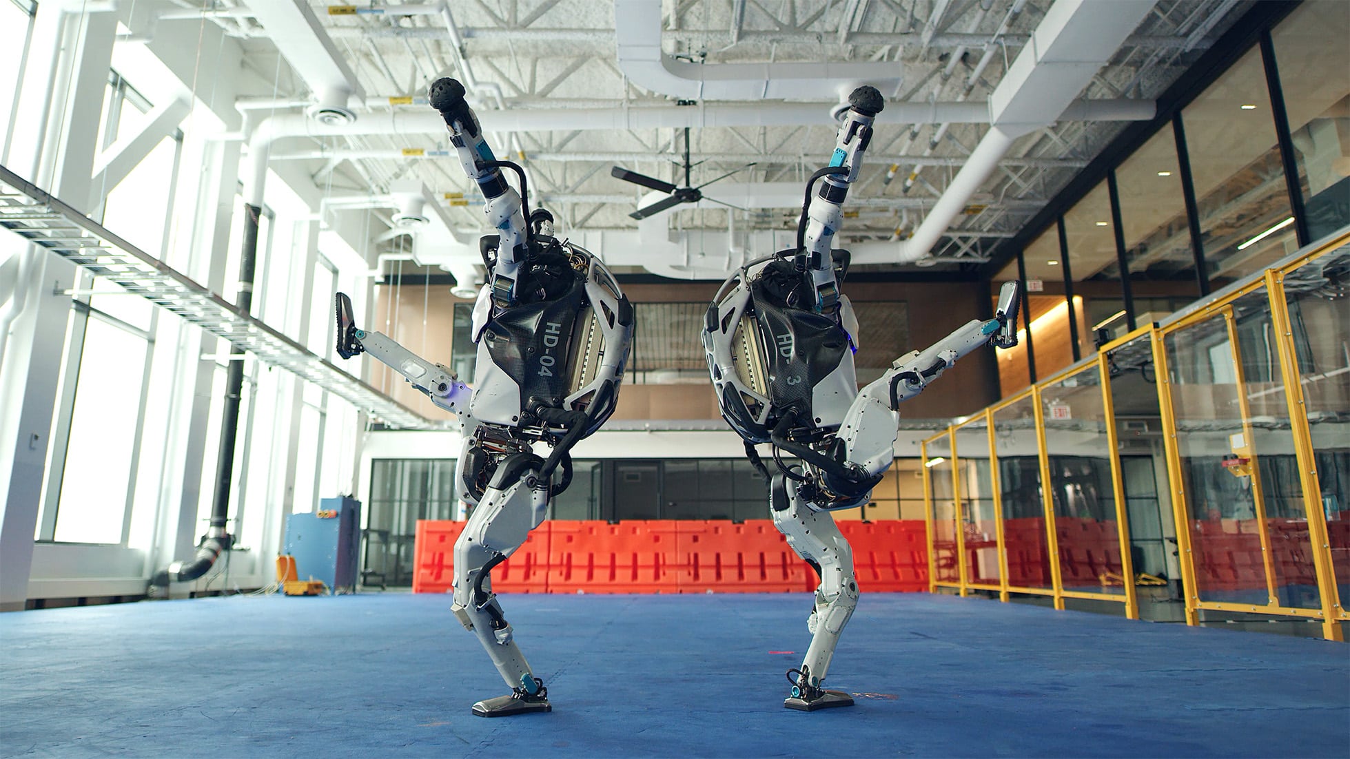 Two Atlas robots dance, standing back to back each with one leg raised