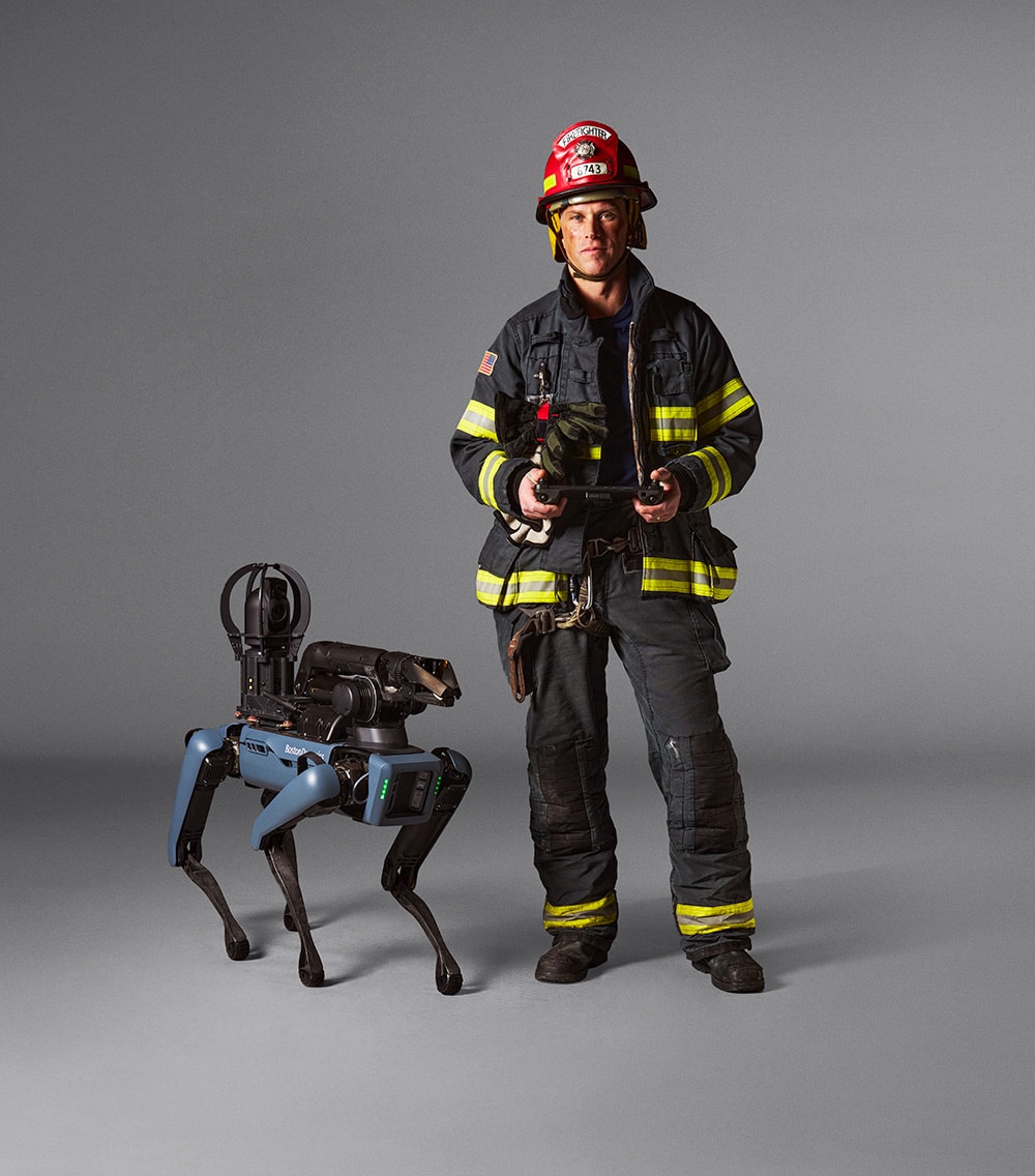 A fire fighter stands next to Spot holding the tablet controller