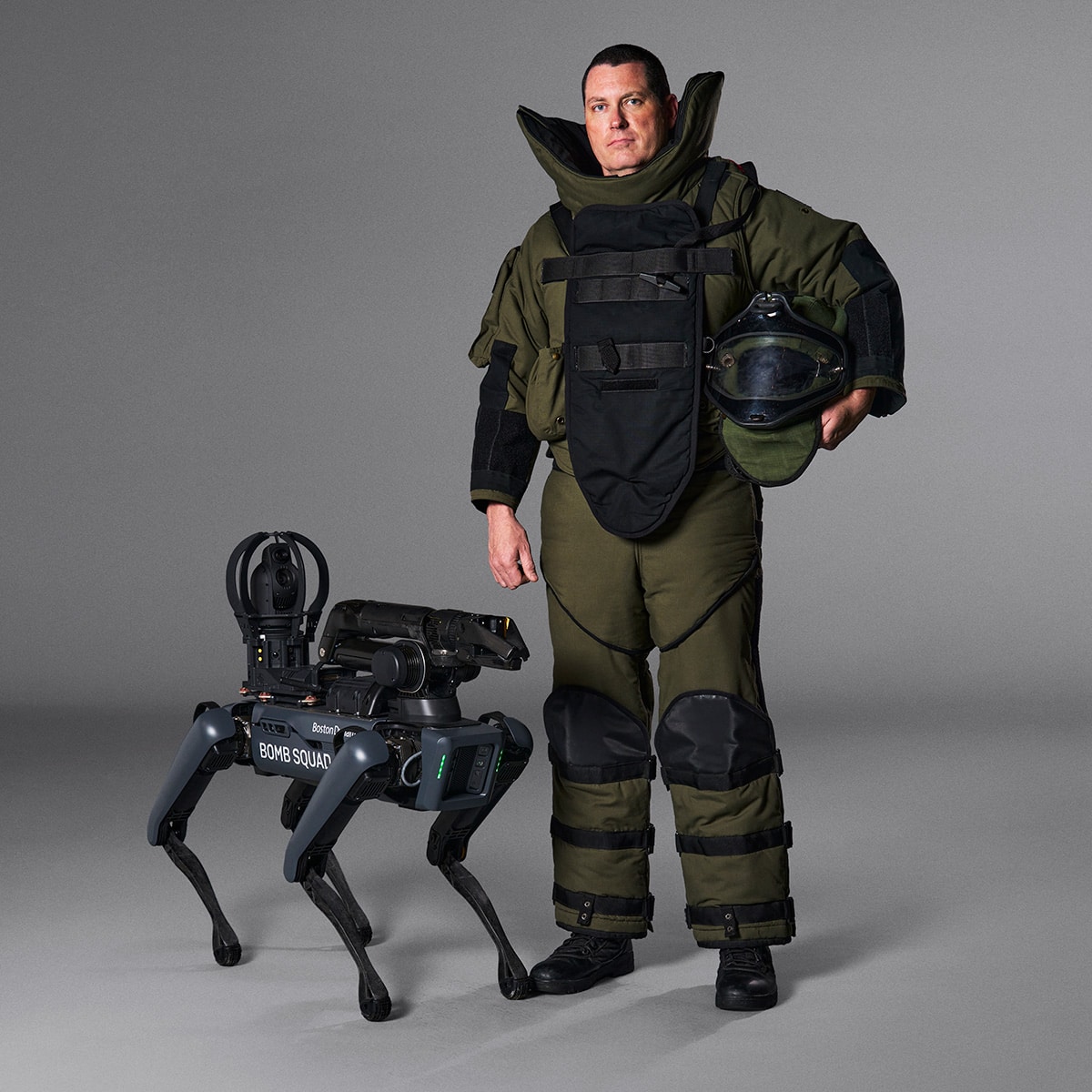 A bomb disposal technician wearing protective gear poses next to the Spot robot