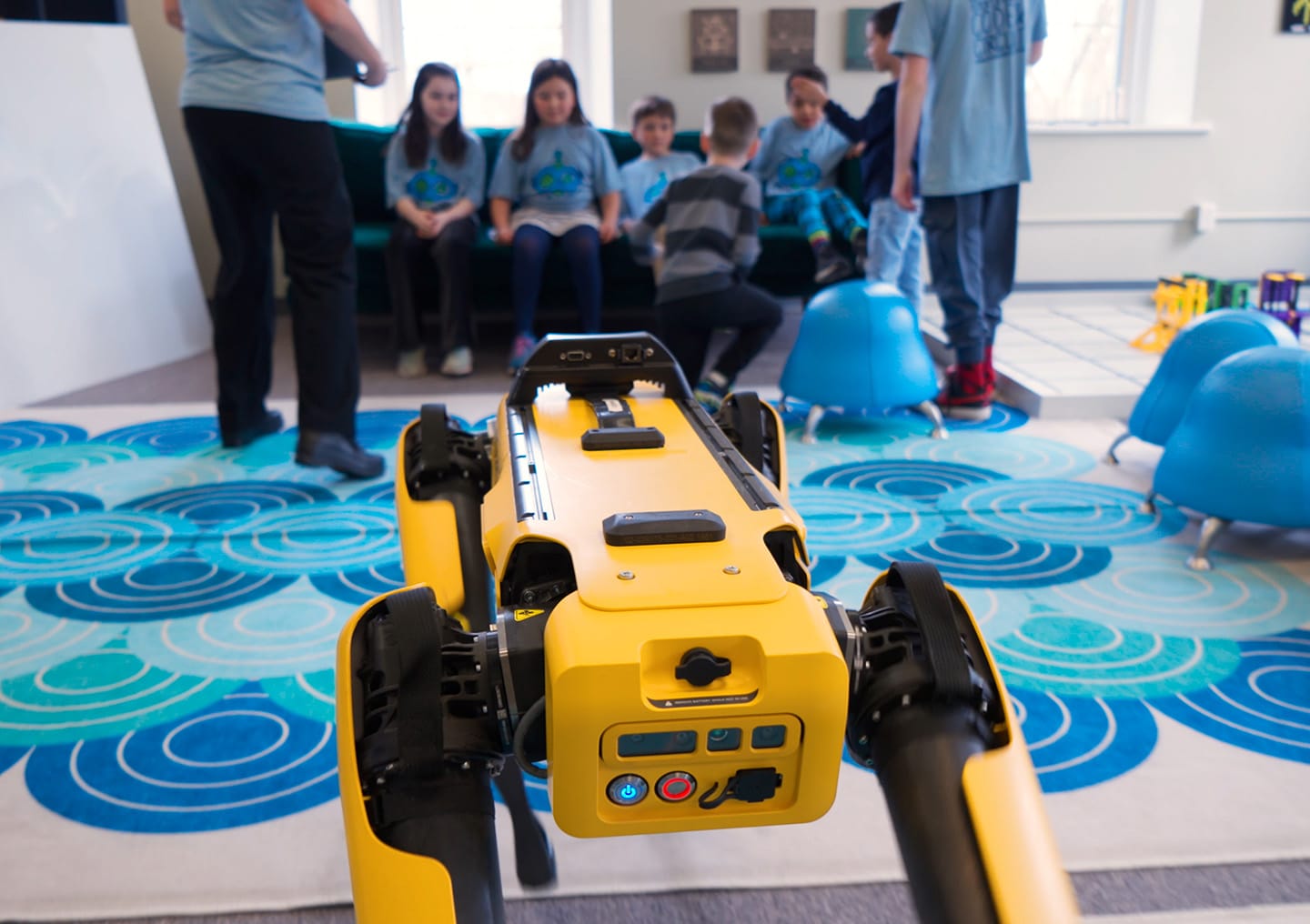 Spot walks through a classroom while young students watch