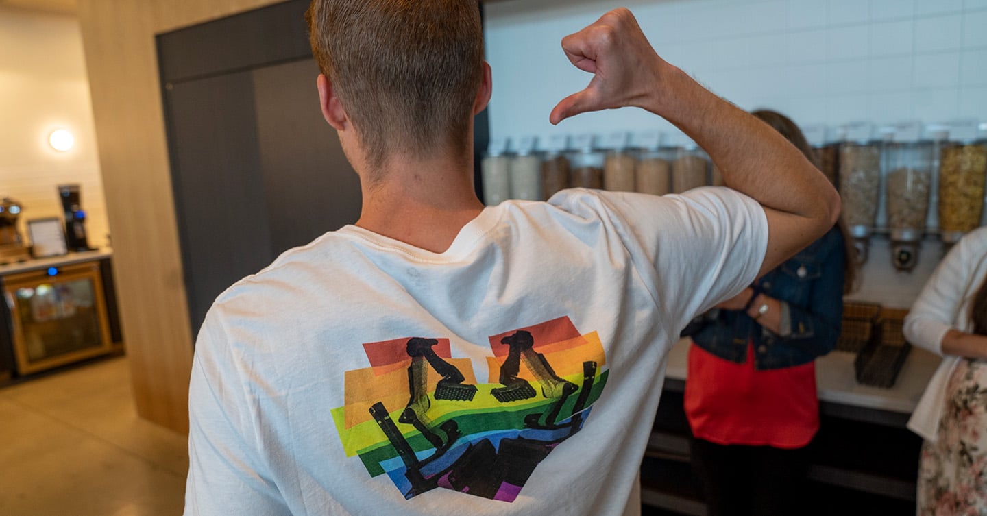 An employee facing away from camera gestures to a 2 robots in rainbow heart on their shirt