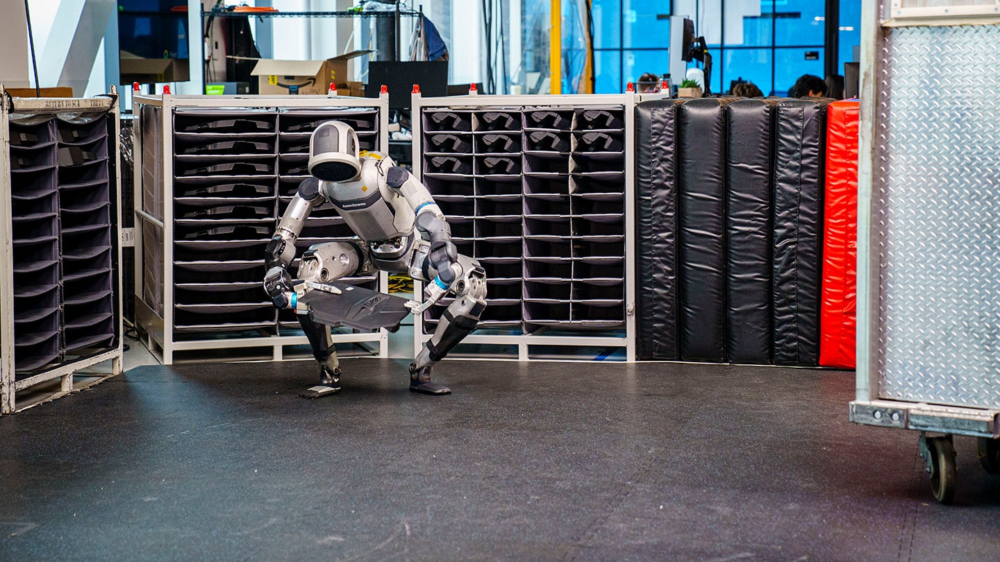 the Atlas robot squats deeply to lift an object from the floor with both hands