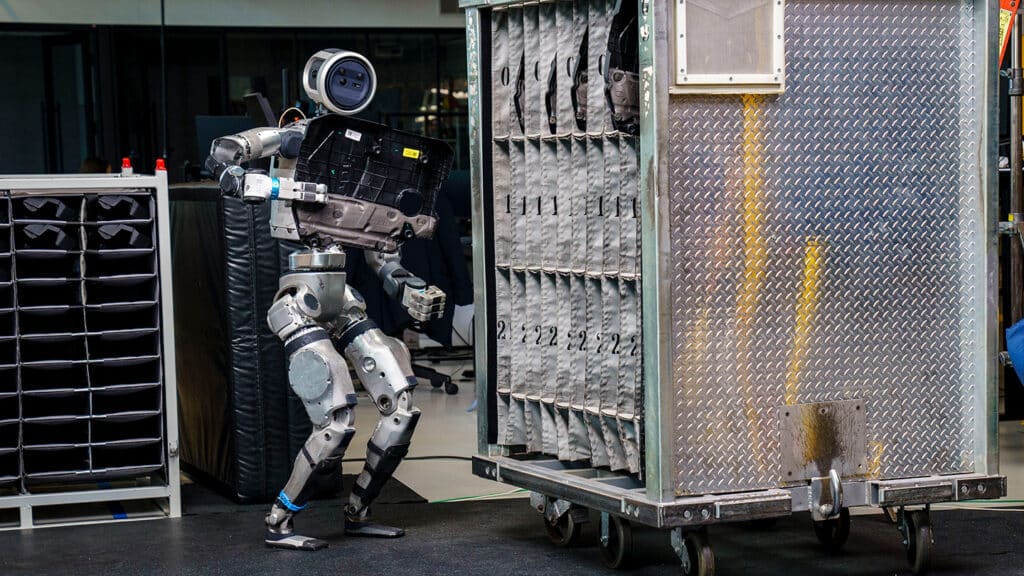 The Atlas humanoid robot places an engine cover into a mobile sequencing container
