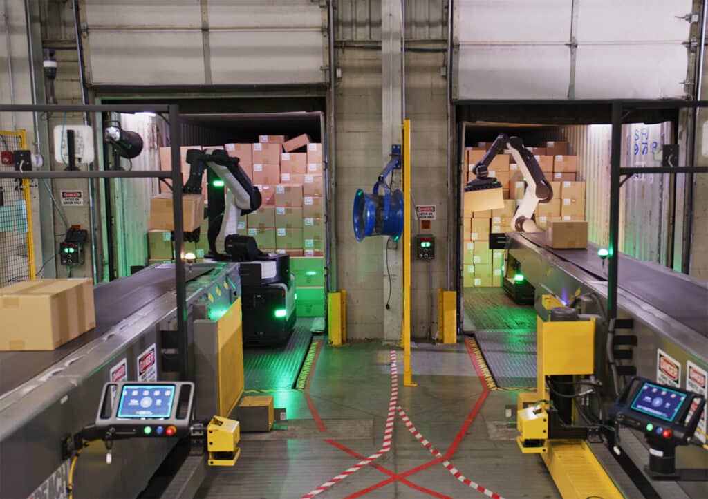 Two robots unload boxes to conveyor belts in a warehouse.