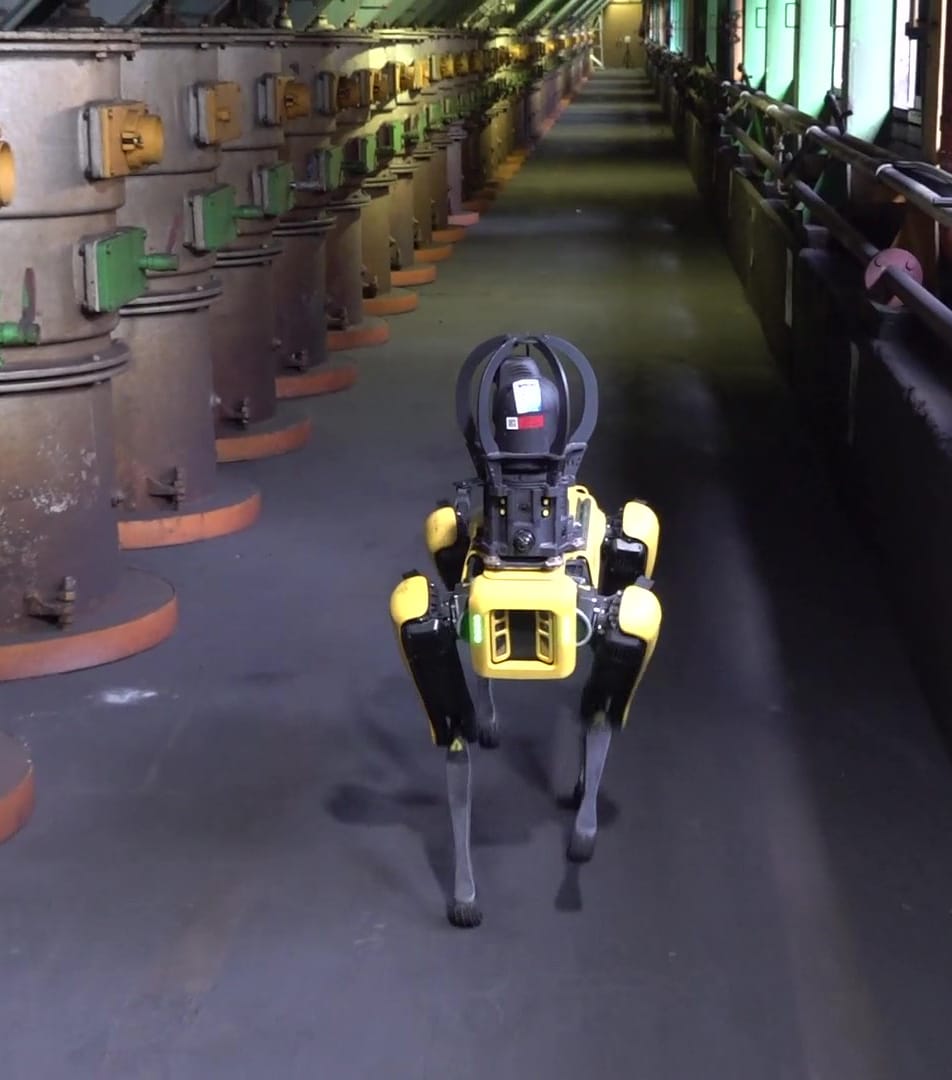 A yellow Spot robot equipped for inspection walks through a steel plant