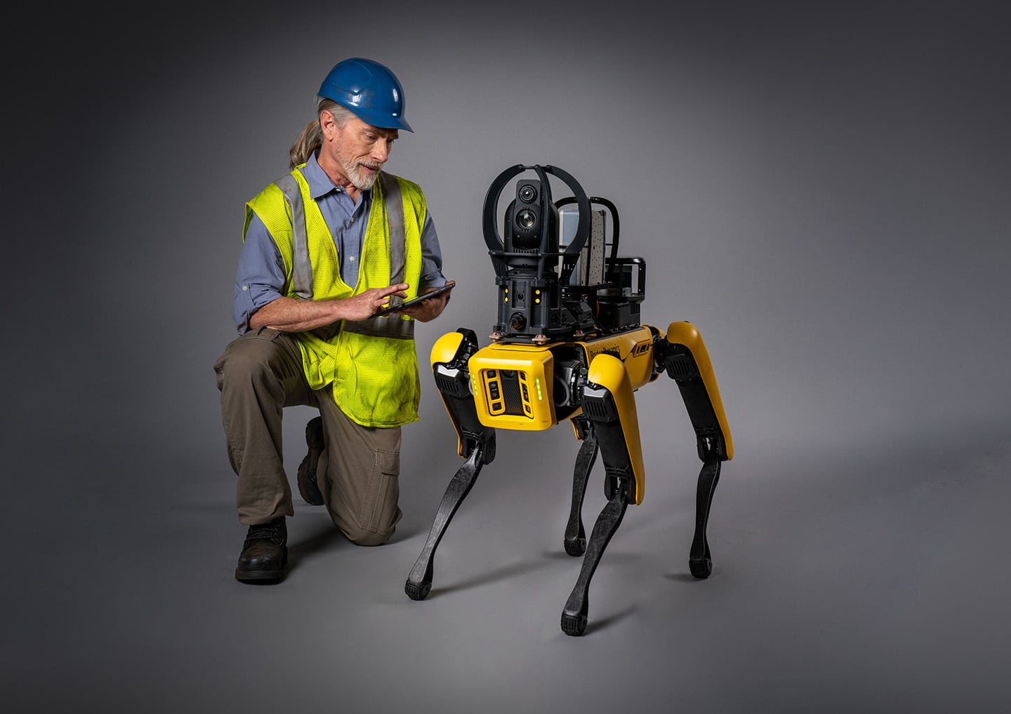 An operator kneels next to Spot adjusting settings on the tablet controller