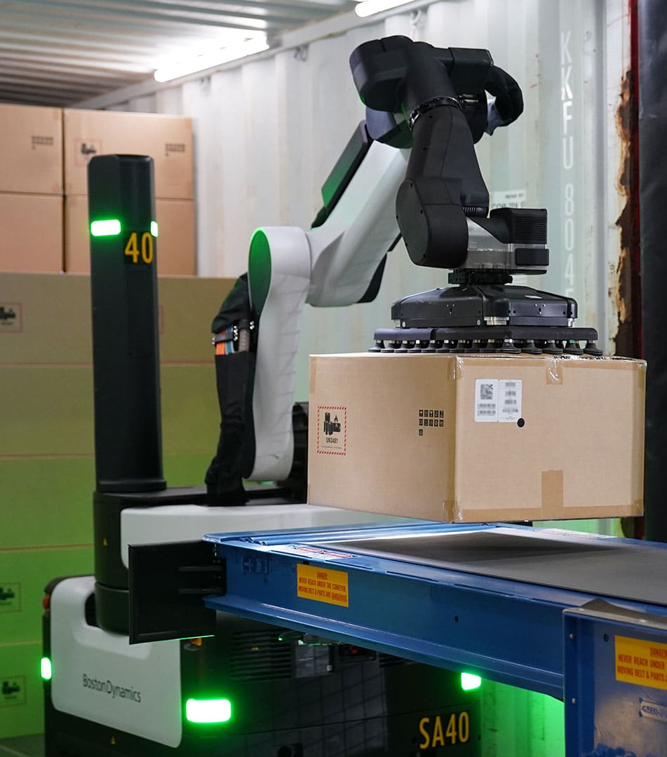 Robot holds large box with its suction gripper over a conveyor