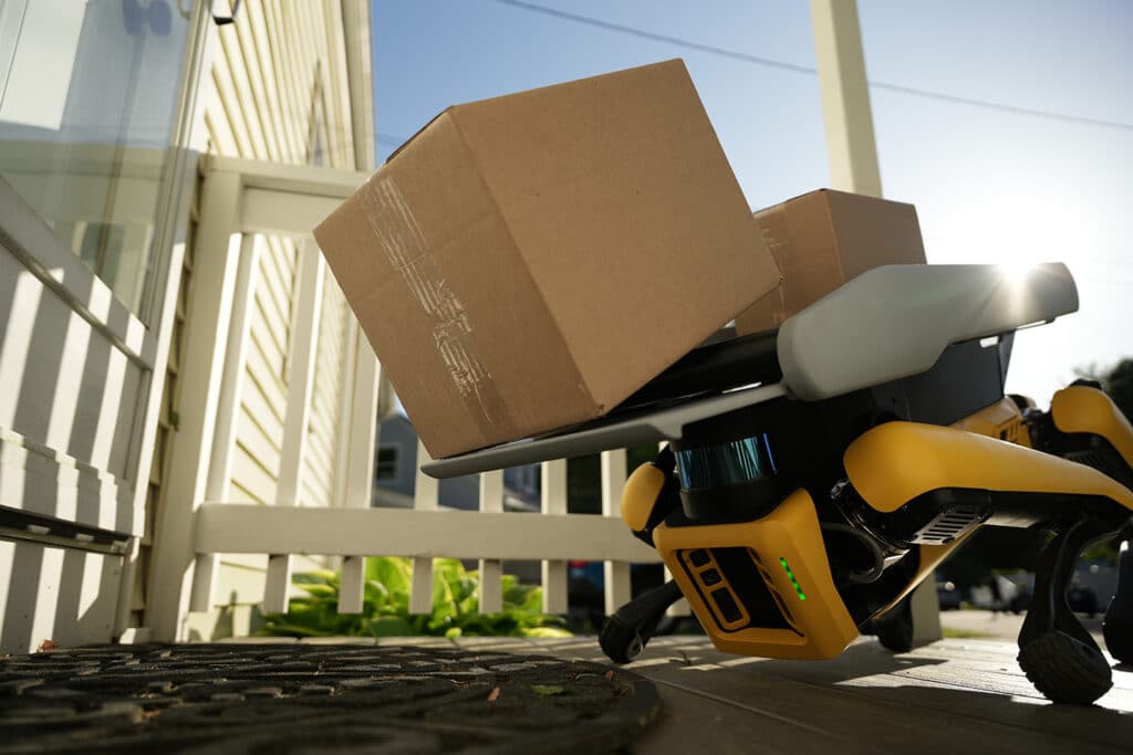 A Spot robot crouches to deposit a package onto a suburban porch
